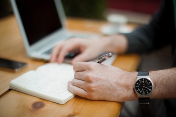 Person writing next to laptop